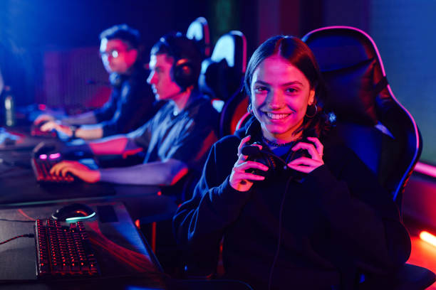 esports gaming team pc players arena Group of esports gamers sitting at PCs in a dark arena, wearing headsets and playing together under neon blue and pink lighting.