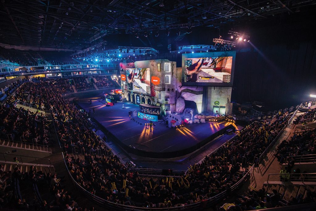 esports stadium crowd live gaming tournament Large esports stadium filled with cheering crowd watching a live gaming tournament on a massive stage and giant screens.